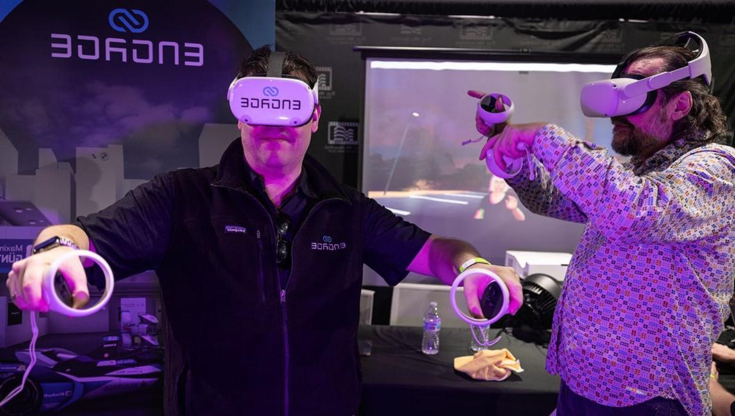 Two men wear virtual reality headsets. They both have their arms extended upward and seem to be enjoying themselves.